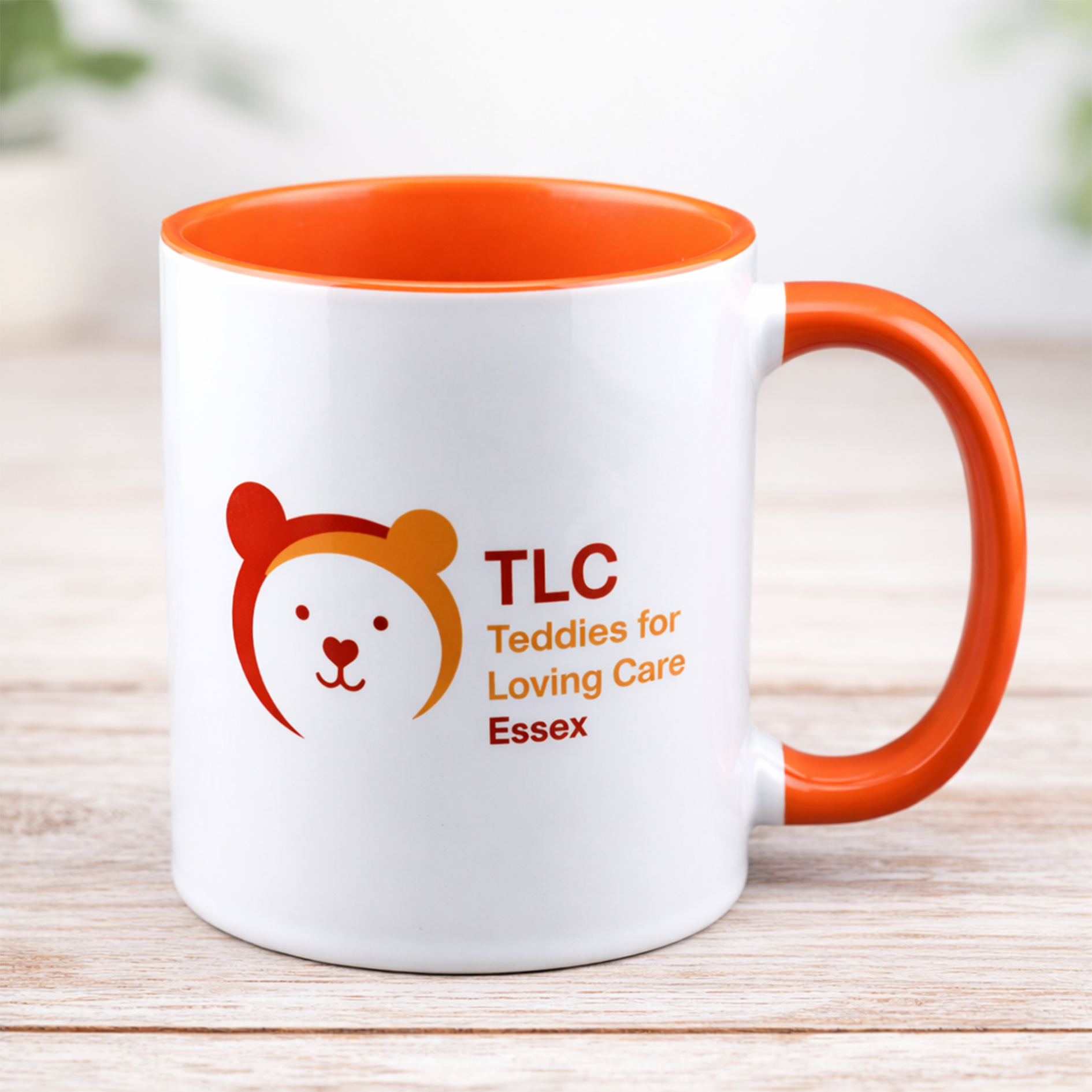 White mug with an orange handle and the TLC Teddies for Loving Care Essex logo